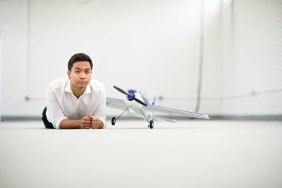 Anirudha Majumdar lying on the ground next to a model airplane.