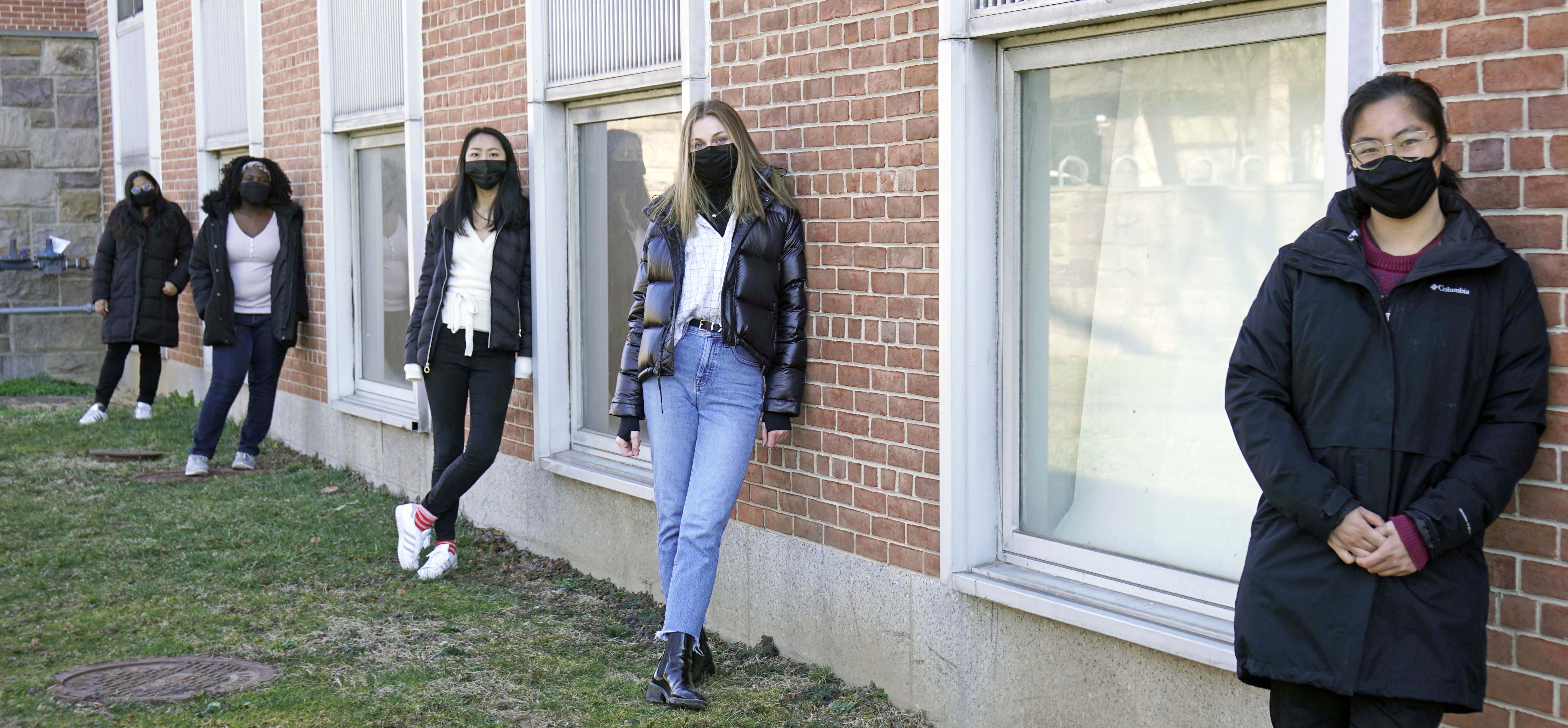 Photo of five students standing along a wall outside of a building at E-Quad.