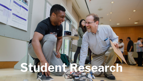 student working on a robot smiling at a professor